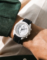 Black rubber strap with white stitching fitted to an OMEGA x Swatch MoonSwatch Mission to the Moonphase watch, worn on the wrist in a lifestyle shot with clothing visible