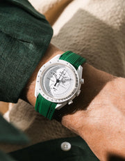 Green rubber strap fitted to an OMEGA x Swatch MoonSwatch Mission to the Moonphase watch, worn on the wrist in a lifestyle shot with clothing visible