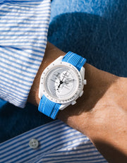 Neptune Blue rubber strap fitted to an OMEGA x Swatch MoonSwatch Mission to the Moonphase watch, worn on the wrist in a lifestyle shot with clothing visible