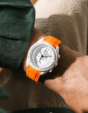 Orange rubber strap fitted to an OMEGA x Swatch MoonSwatch Mission to the Moonphase watch, worn on the wrist in a lifestyle shot with clothing visible