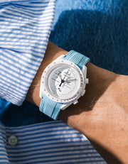 Turquoise rubber strap fitted to an OMEGA x Swatch MoonSwatch Mission to the Moonphase watch, worn on the wrist in a lifestyle shot with clothing visible
