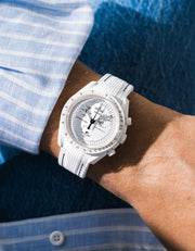 White rubber strap with black stitching fitted to an OMEGA x Swatch MoonSwatch Mission to the Moonphase watch, worn on the wrist in a lifestyle shot with clothing visible