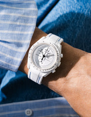 White rubber strap with blue stitching fitted to an OMEGA x Swatch MoonSwatch Mission to the Moonphase watch, worn on the wrist in a lifestyle shot with clothing visible